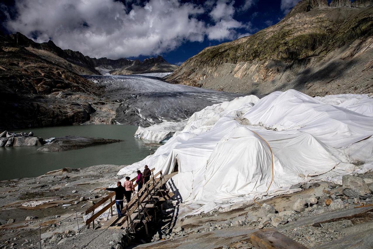 FILE PHOTO: Tourists stand outside the ice cave covered with protection material preventing the ice from melting at the Rhone Glacier in Obergoms