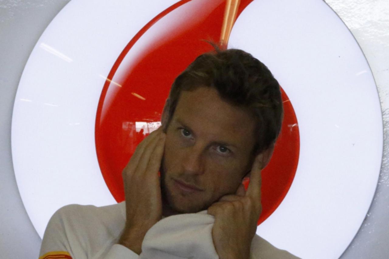 'McLaren Formula One driver Jenson Button of Britain covers his ears inside his garage during the third practice session of the Abu Dhabi F1 Grand Prix at the Yas Marina circuit on Yas Island November