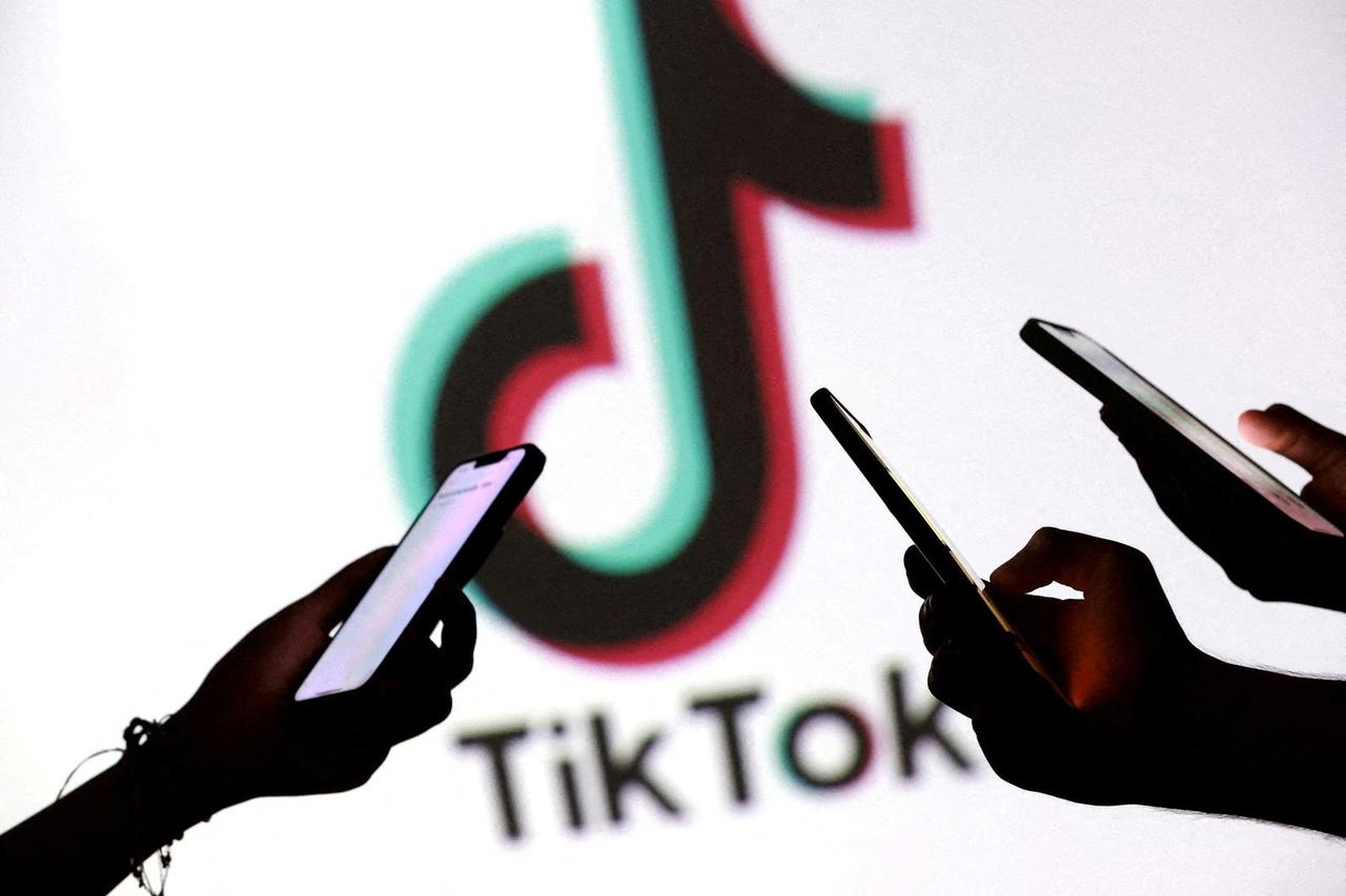 FILE PHOTO: Illustration shows teenagers pose for a photo while holding smartphones in front of a TikTok logo