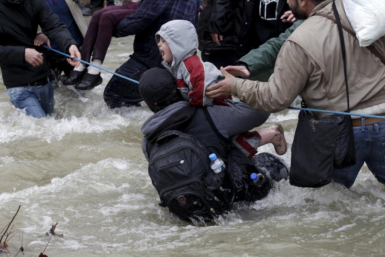 A migrant tries to stop a child from falling in the water as migrants wade across a river near the Greek-Macedonian border, west of the the village of Idomeni, Greece, March 14, 2016. REUTERS/Alexandros Avramidis      TPX IMAGES OF THE DAY     