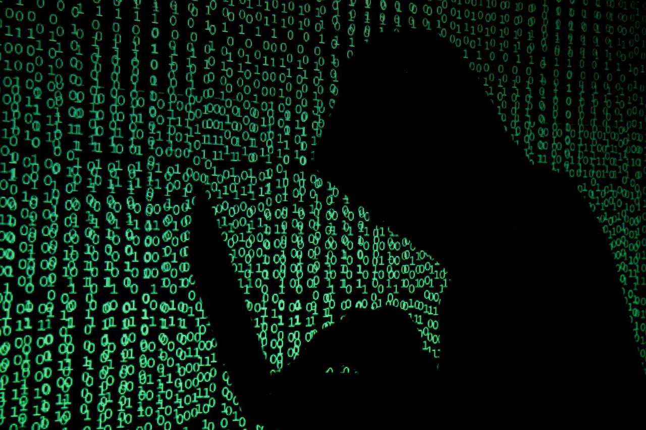 FILE PHOTO: Hooded man holds laptop computer as cyber code is projected on him in this illustration picture