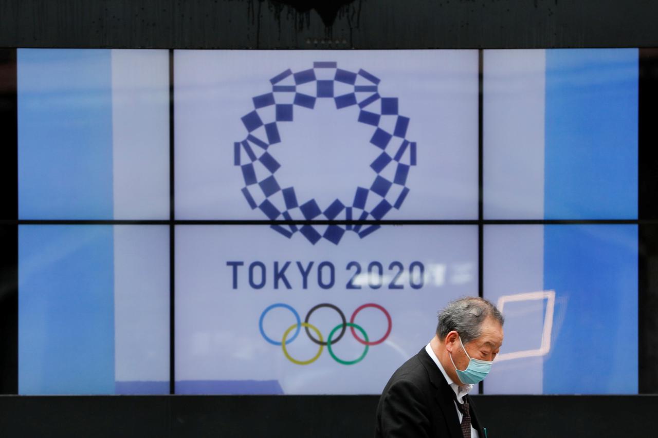 FILE PHOTO: A passerby wearing a protective face mask walks past a screen showing the logo of the Tokyo 2020 Olympic Games in Tokyo