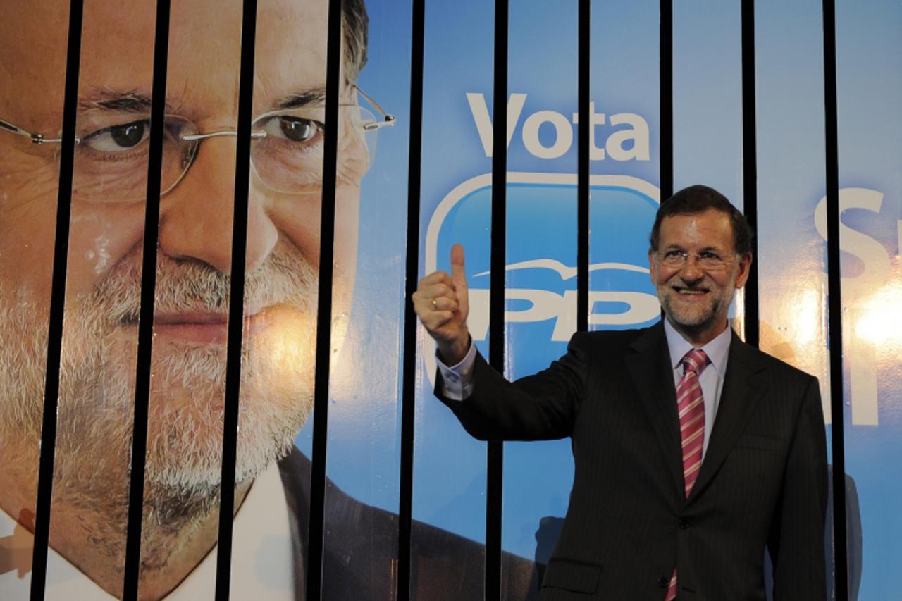 'Leader of the Spanish opposition party Partido Popular (PP) and candidate for general elections, Mariano Rajoy gives the thumb up in front of an election poster during a meeting marking the start of 