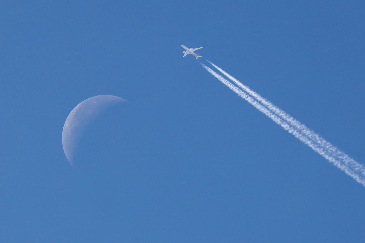 A passenger plane flies in the sky past the moon in the background over Belgrade