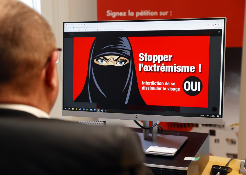 Swiss National Councillor Addor looks on his computer at a poster reading "Stop Extremism!" in Sion
