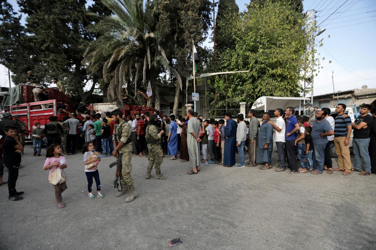 FILE PHOTO: People stand in a queue to get bread in the border town of Tal Abyad