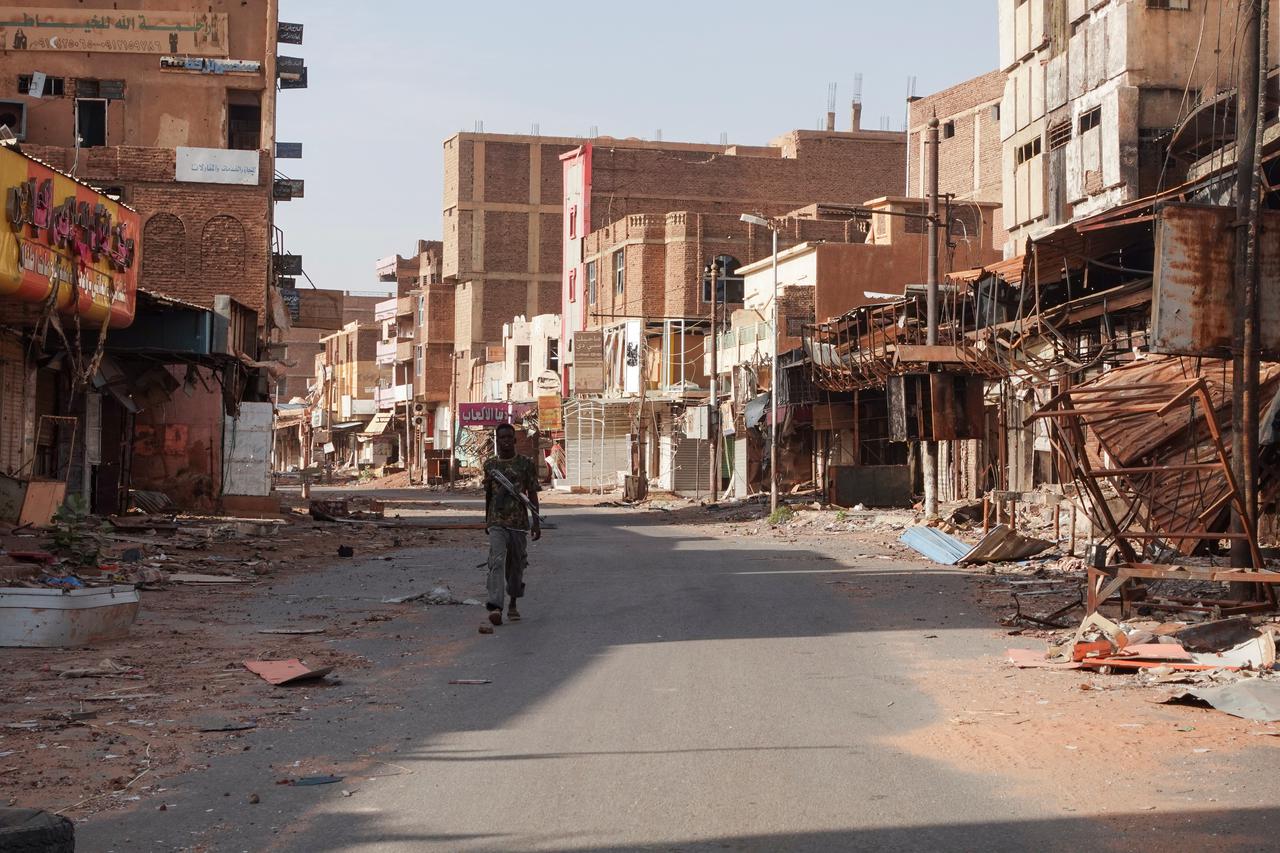 A member of the Sudanese Armed forces walks between damaged buildings, in Omdurman