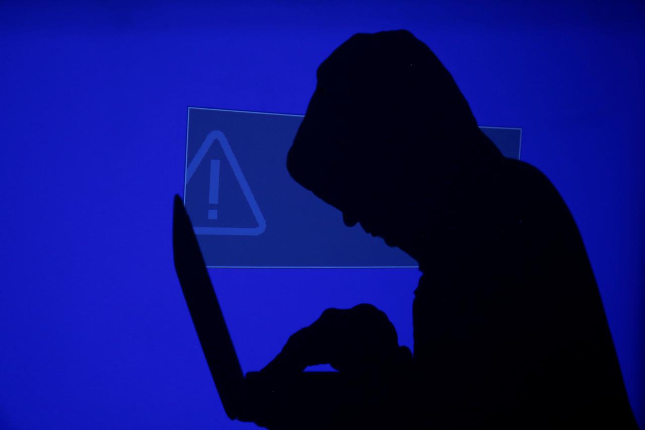 FILE PHOTO: Hooded man holds laptop computer as blue screen with an exclamation mark is projected on him in this illustration picture