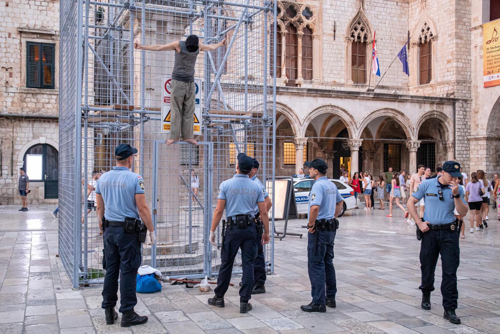 04.09.2022., Orlandov stup, Dubrovnik - Nepoznati ‘performer‘ koji je glavu sakrio popeo se na ogradu kojom je zasticen spomenik Orlando u povijesnoj jezgri Dubrovnika. Muskarac je mirno stajao na ogradi vise od pola sata, nije komunicirao niti je poznato što je svojim postupkom zeli poruciti ili postici. No, na njegov je performas reagirala policija. Dva policajca nisu ga uspjela nagovoriti da se spusti, no uz pojacanje muskarac je spusten s ograde i odvezen u policijskom vozilu.  Photo: Grgo Jelavic/PIXSELL
