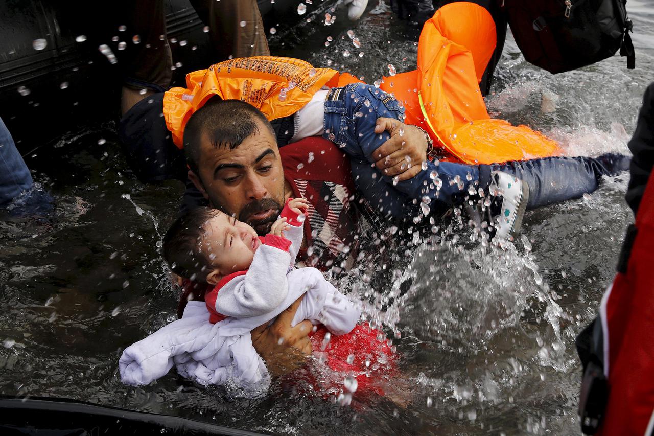 A Syrian refugee holds onto his children as he struggles to walk off a dinghy on the Greek island of Lesbos, after crossing a part of the Aegean Sea from Turkey to Lesbos September 24, 2015.  REUTERS/Yannis Behrakis          SEARCH 