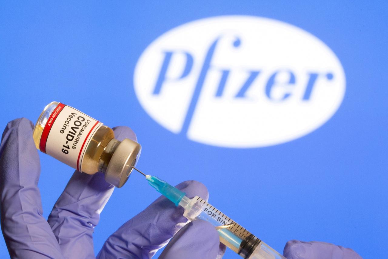 FILE PHOTO: A woman holds a small bottle labeled with a "Coronavirus COVID-19 Vaccine" sticker and a medical syringe in front of displayed Pfizer logo in this illustration