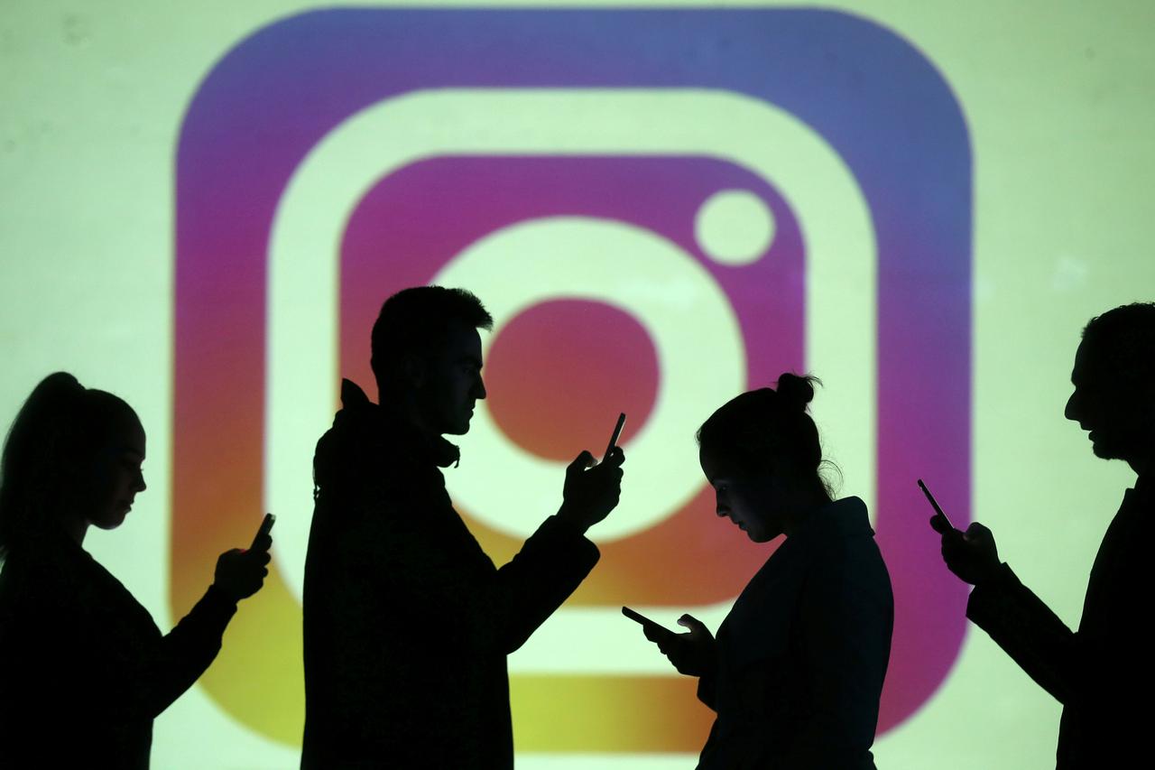 FILE PHOTO: Silhouettes of mobile users are seen next to a screen projection of the Instagram logo in this picture illustration