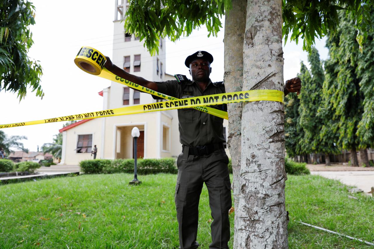 A police officer ties a crime scene tape following an attack on worshippers by gunmen at St. Francis Catholic Church in Owo