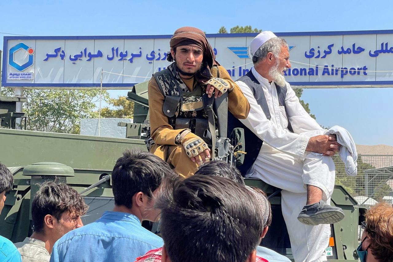 A member of Taliban forces (L) sits on a an armoured vehicle outside Hamid Karzai International Airport in Kabul