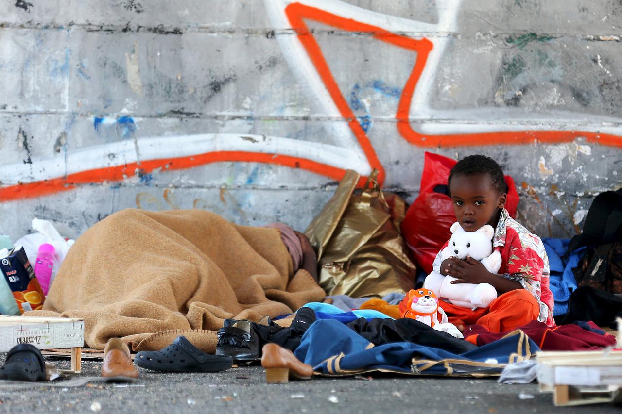 A child sits on the street as his mother (L) sleeps next to the Tiburtina station in Rome, June 11, 2015. Hundreds of migrants brought to Italy after being rescued at sea in recent weeks camped along the streets near Rome's Tiburtina train station and gat