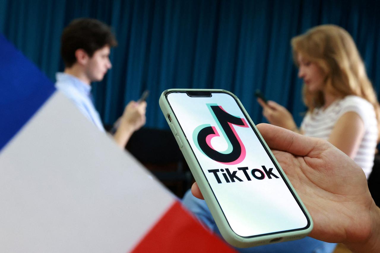Illustration shows teenagers pose for a photo next to a France flag while holding smartphones with a TikTok logo