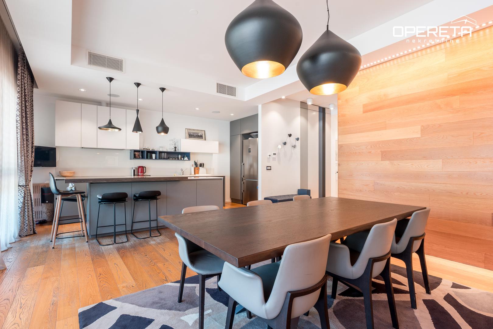 Zapadna orijentacija donosi obilje prirodnog svjetla, a prostrani open space dnevni boravak povezan s kuhinjom i blagovaonicom stvara dojam elegancije i prozračnosti. Kamin dodatno naglašava toplinu prostora, dok velika staklena stijena pruža otvoren pogled i poseban ugođaj tijekom cijele godine.

