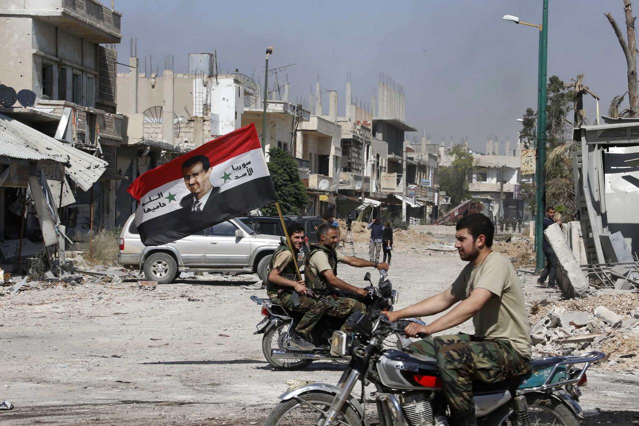 Forces loyal to Syria's President Bashar al-Assad carry the national flag as they ride on motorcycles in Qusair, after the Syrian army took control from rebel fighters in this June 5, 2013 file photograph. The civil war that has unfolded in Syria over the