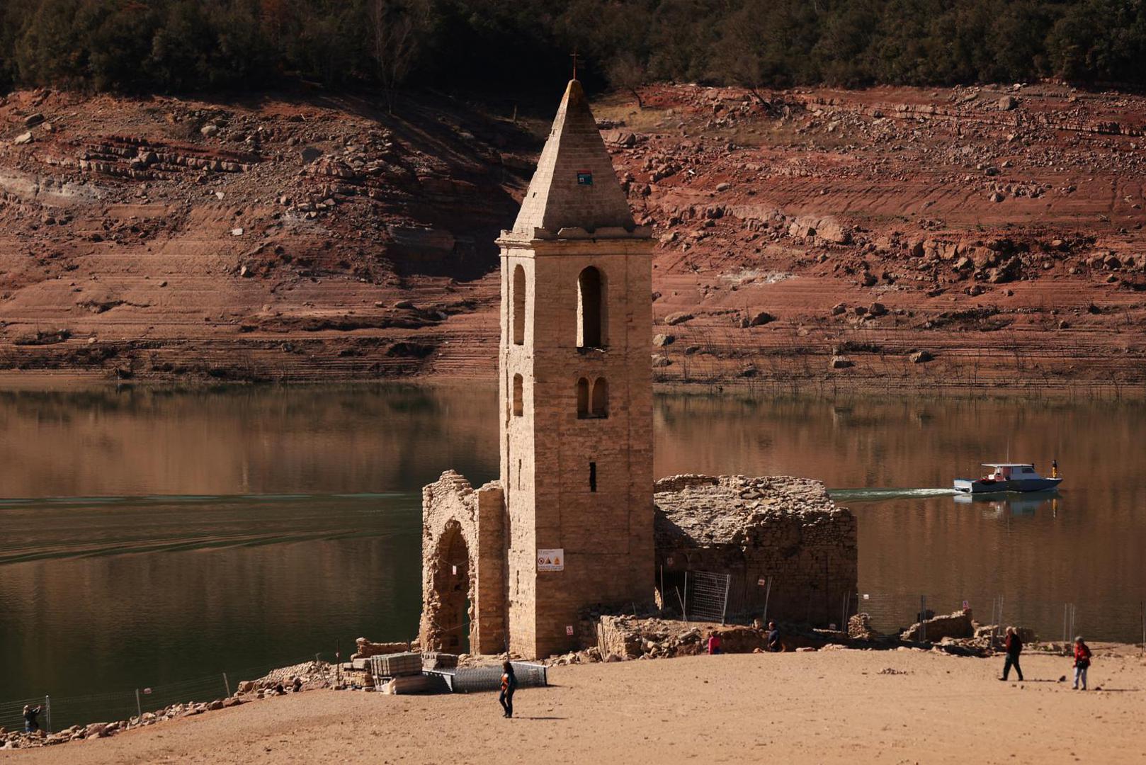 Tourists walk while fishermen collect fish from the Sau reservoir next to a church of the village of San Roman de Sau after its re-emerging as Sau reservoir has lowest level since 1990 due to extreme drought in Catalonia, near Vic, Spain March 15, 2023. REUTERS/Nacho Doce Photo: NACHO DOCE/REUTERS