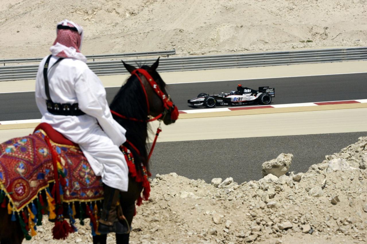 'Abdel Rouf, a member of the Bahrainian Royal Arab Studs, watches Minardi\'s driver Patrick Friesacher of Austria driving past on the back of his horse Tuwasian during the fourth practice session for 