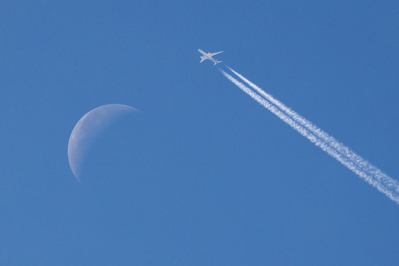 A passenger plane flies in the sky past the moon in the background over Belgrade