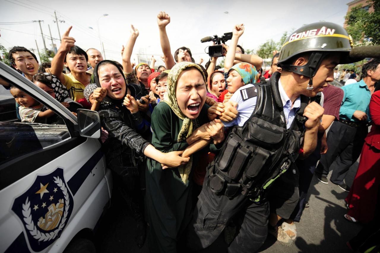 'YEARENDER 2009 Ethnic Uygur women grab a riot policemen as they protest in Urumqi in China\'s far west Xinjiang province on July 7, 2009.   Police fired clouds of acrid tear gas to disperse thousands