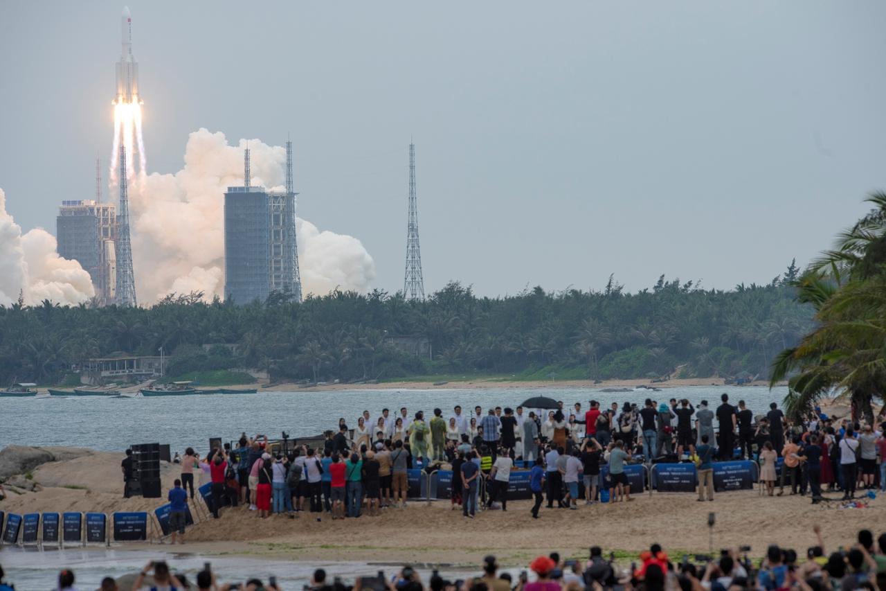 FILE PHOTO: People watch from a beach as the Long March-5B Y2 rocket, carrying the core module of China's space station Tianhe, takes off from Wenchang