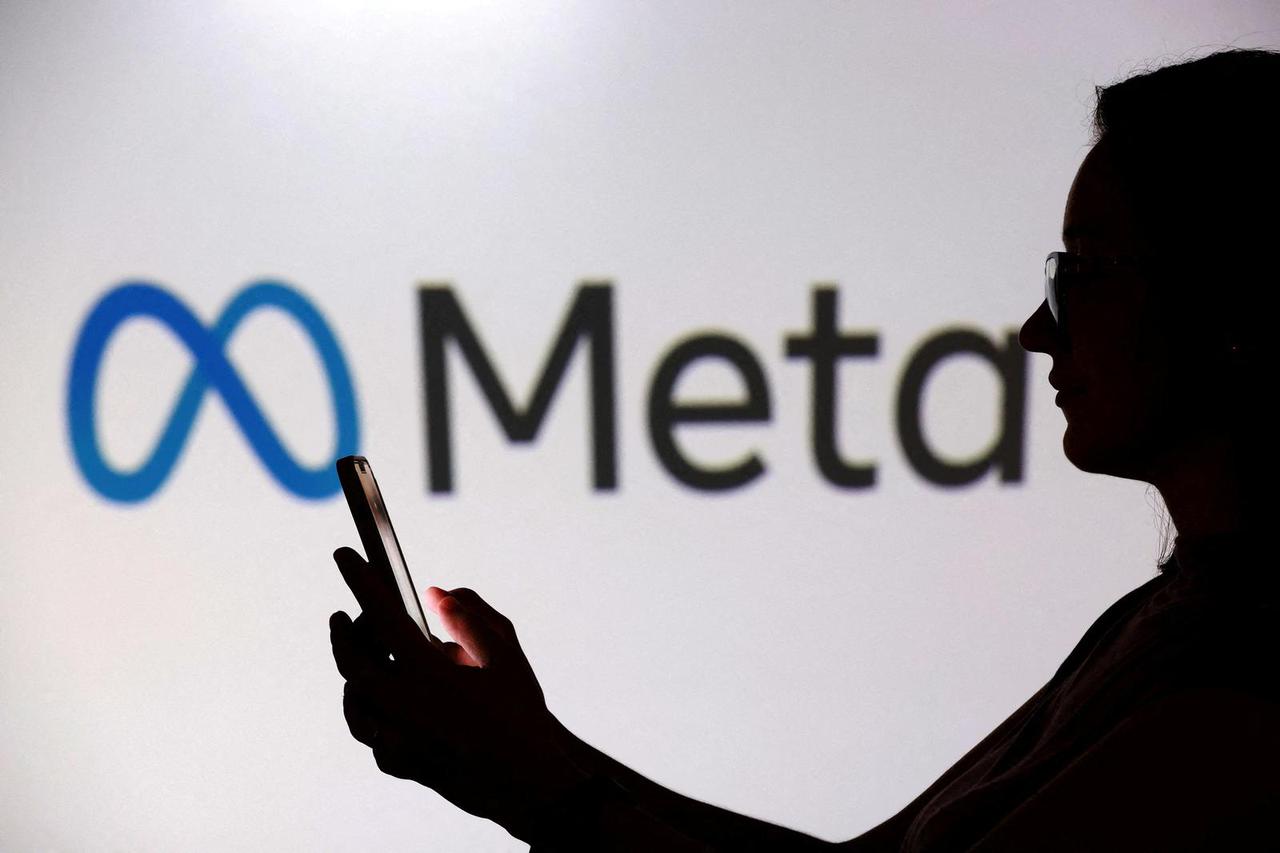 FILE PHOTO: Illustration shows a teenager posing for a photo while holding a smartphone in front of a Meta logo