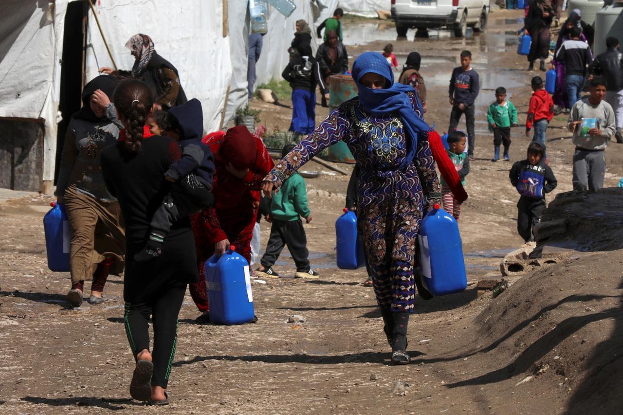 FILE PHOTO: Syrian refugees walk as they carry containers at an informal tented settlement in the Bekaa valley