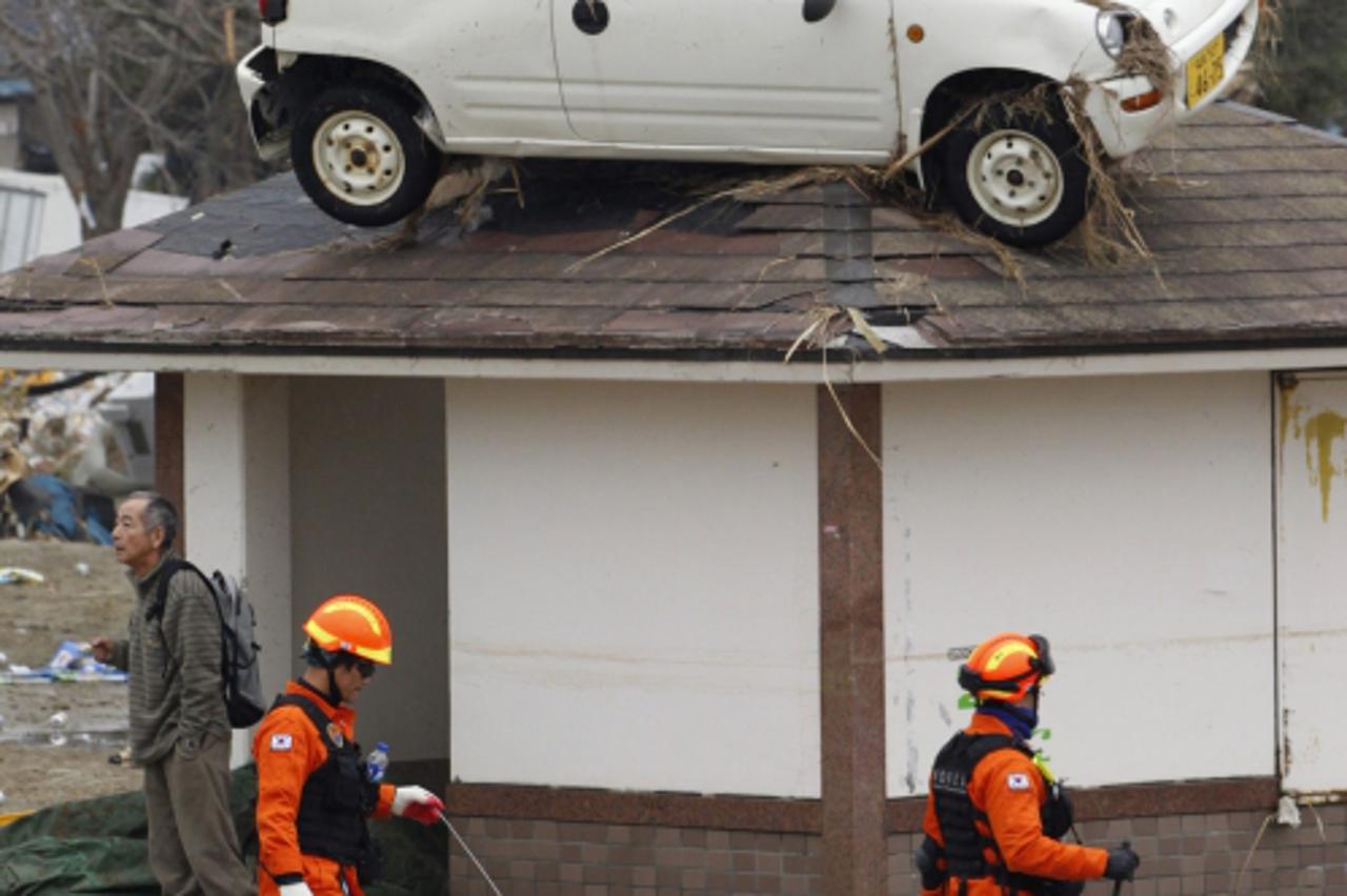 \'A car is seen on the rooftop of a house as South Korean rescue workers walk past it in an area hit by an earthquake and tsunami in Sendai, northeastern Japan March 15, 2011.  REUTERS/Jo Yong-Hak (JA