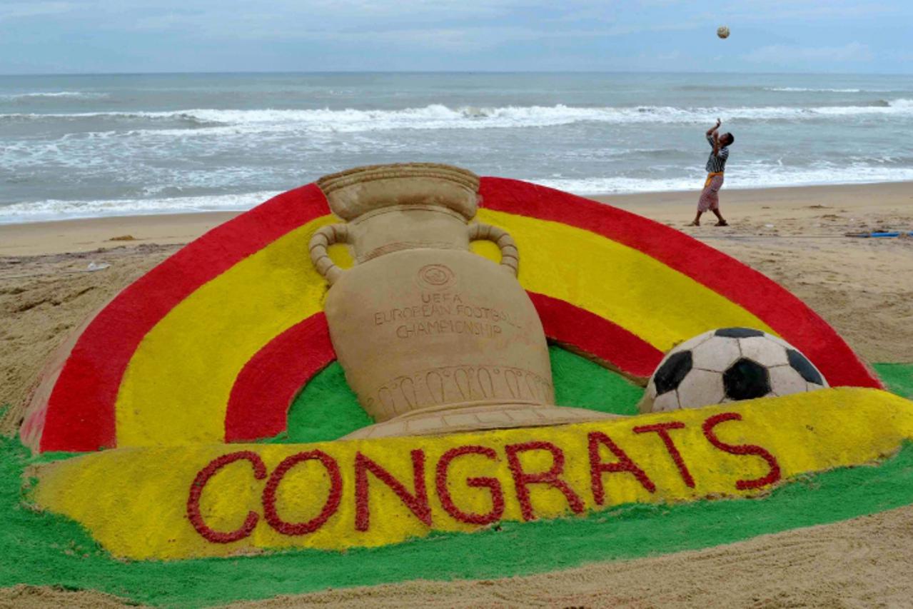 'An Indian boy plays with a football behind a sand sculpture created by international sand artist Sudarsan Pattnaik in order to congratulate the Spanish football team on winning the Euro 2012 football