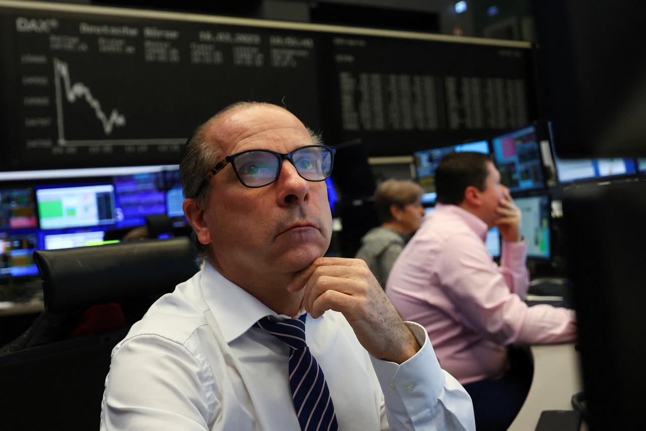 A stock broker looks at his screens in front of the share price index DAX graph following the shares of Credit Suisse hit a record low