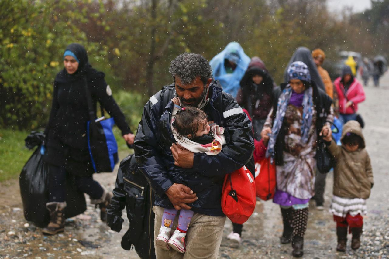A migrant carries his child after crossing the border from Greece into Macedonia, near Gevgelija, Macedonia, November 27, 2015. Macedonia, Serbia and other Balkan states have implemented a new policy to filter the flow by granting passage onwards toward W