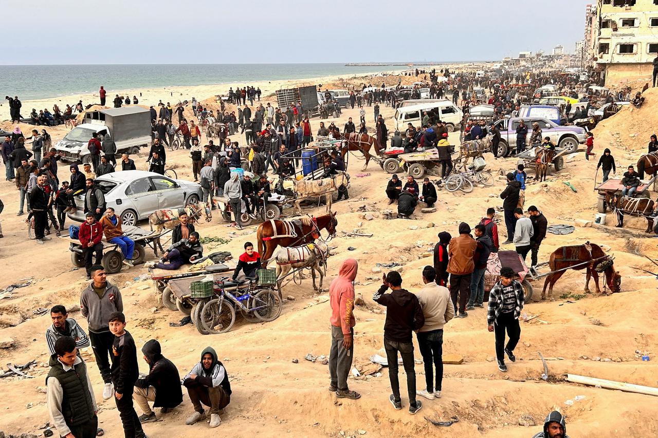 FILE PHOTO: Palestinians gather as they wait for trucks carrying bags of flour to arrive, near an Israeli checkpoint, amid the ongoing conflict between Israel and Hamas, in Gaza City