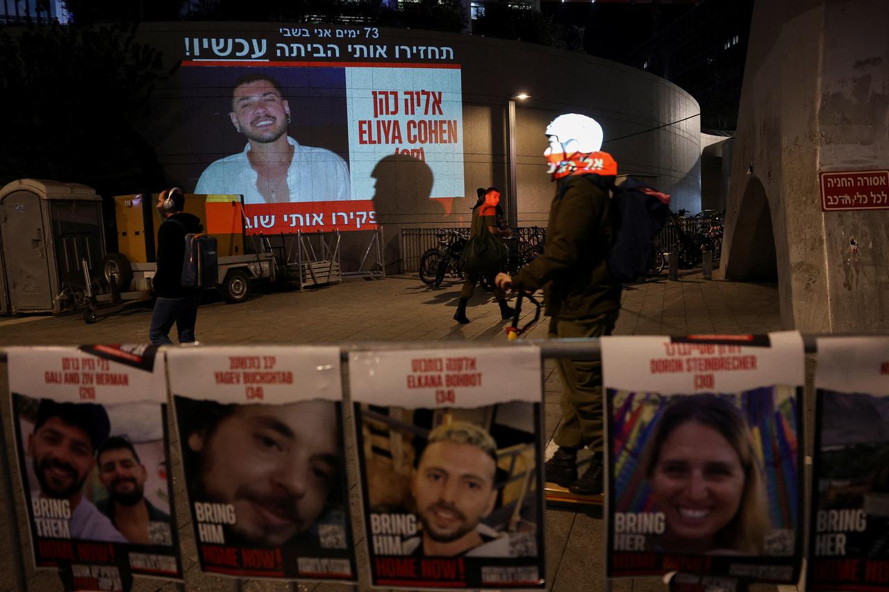A person passes signs with the faces of people being held hostage in Gaza by the Palestinian Islamist group Hamas, in Tel Aviv