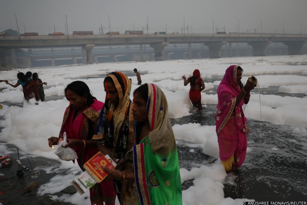Women pray as they stand amidst the foam covering the polluted Yamuna river on a smoggy morning in New Delhi