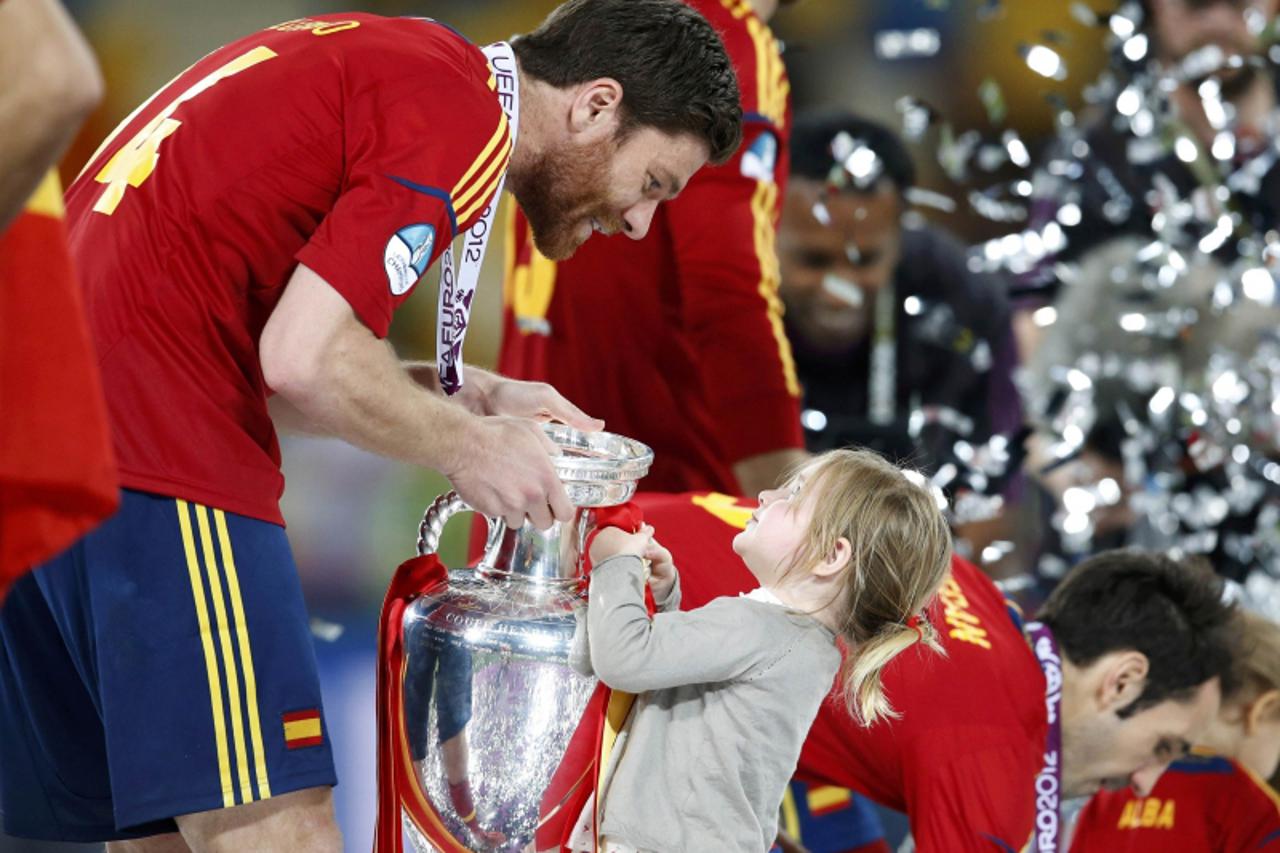 'Spain\'s Xabi Alonso and a child celebrate with the trophy after defeating Italy to win the Euro 2012 final soccer match at the Olympic stadium in Kiev, July 1, 2012.                REUTERS/Alessandr