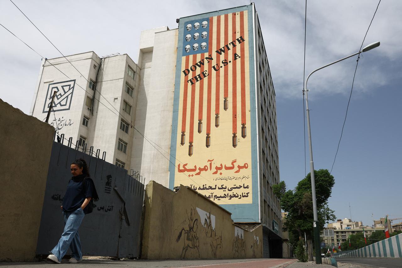 A woman walks past an anti-U.S. mural on a building in Tehran