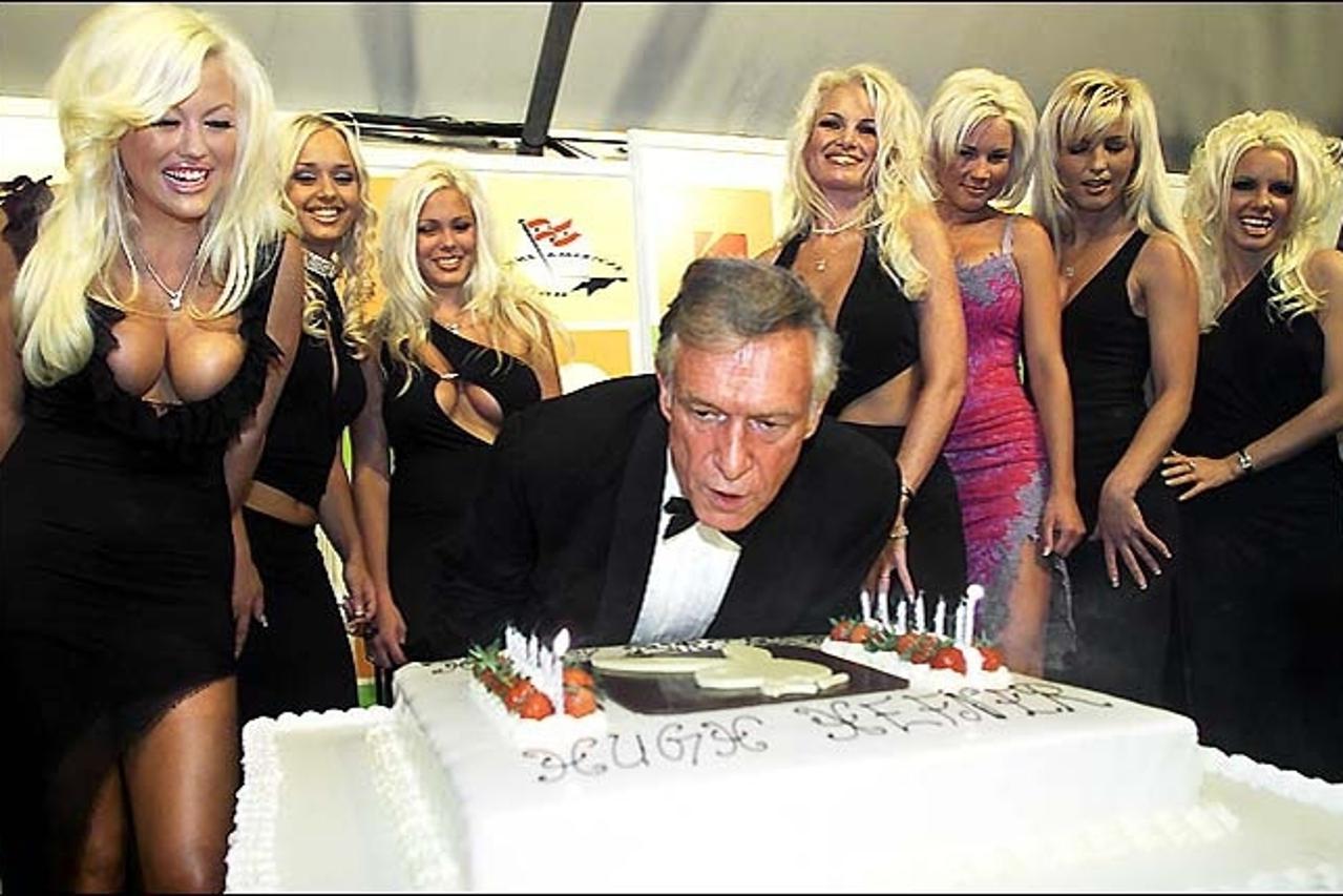 'Caption=Hugh Hefner (C) Playboy founder and Editor-in-Chief, leans over a giant birthday cake as he blows out candles to celebrate his 75th birthday as seven playmates look on in Cannes, May 12, 2001