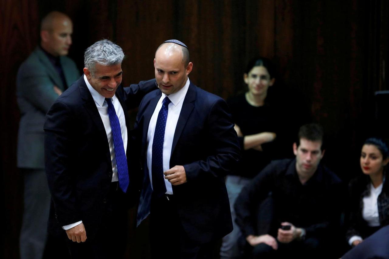 FILE PHOTO: Israel's Finance Minister Lapid and Minister of Economics and Trade Bennett walk together during the swearing-in ceremony at the Israeli Parliament, in Jerusalem