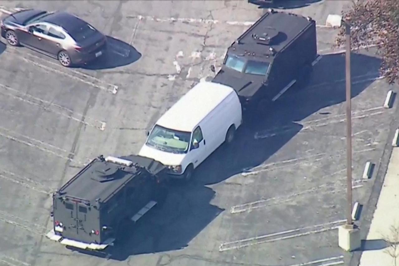 Police use armored vehicles to surround a white cargo van at a parking lot in Torrance