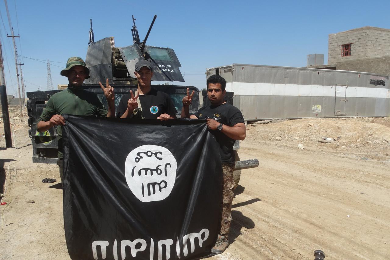 Iraqi security forces stand with an Islamic State flag which they pulled down in the town of Hit in Anbar province, April 2, 2016. 