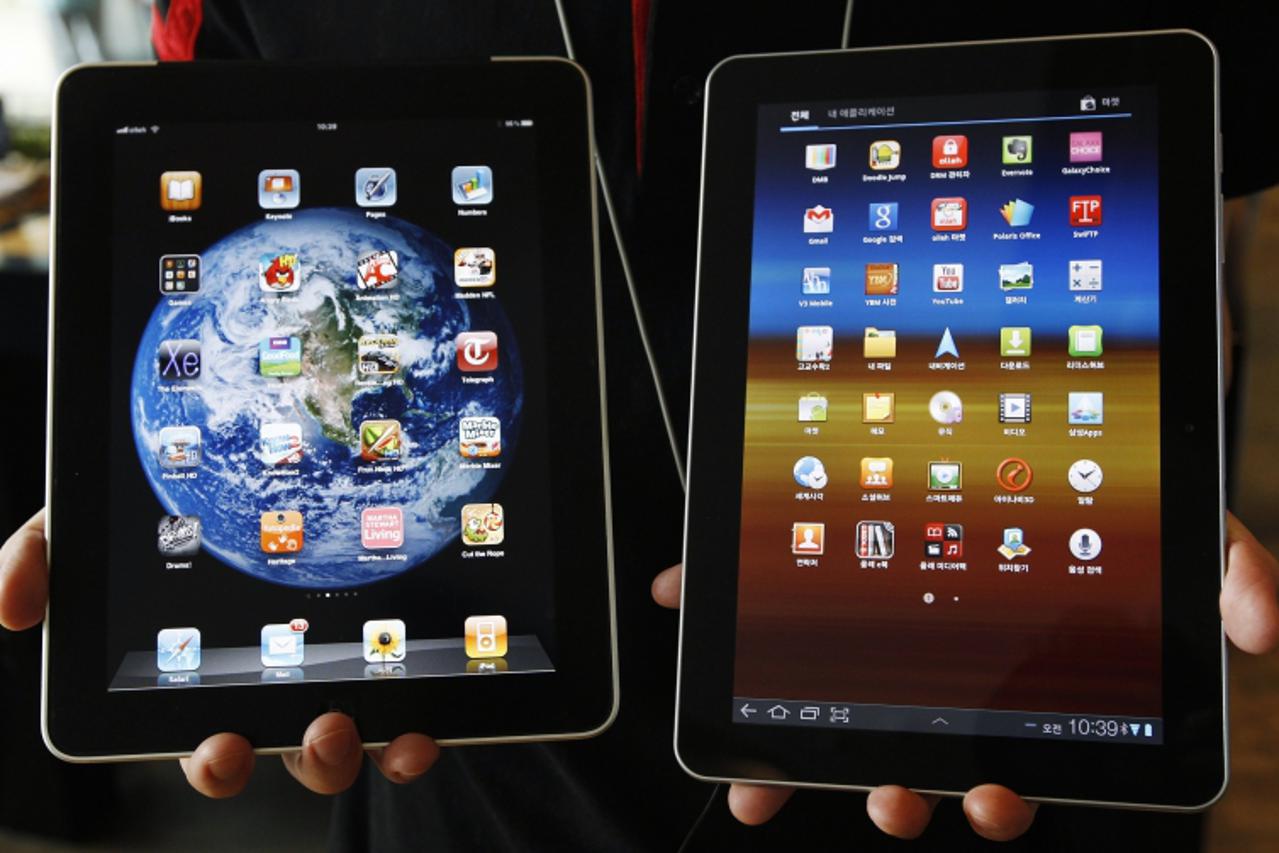 'An employee of South Korean mobile carrier KT holds a Samsung Electronics' Galaxy Tab 10.1 tablet (R) and Apple Inc's iPad tablet as he poses for photos at a registration desk at KT's headquarters