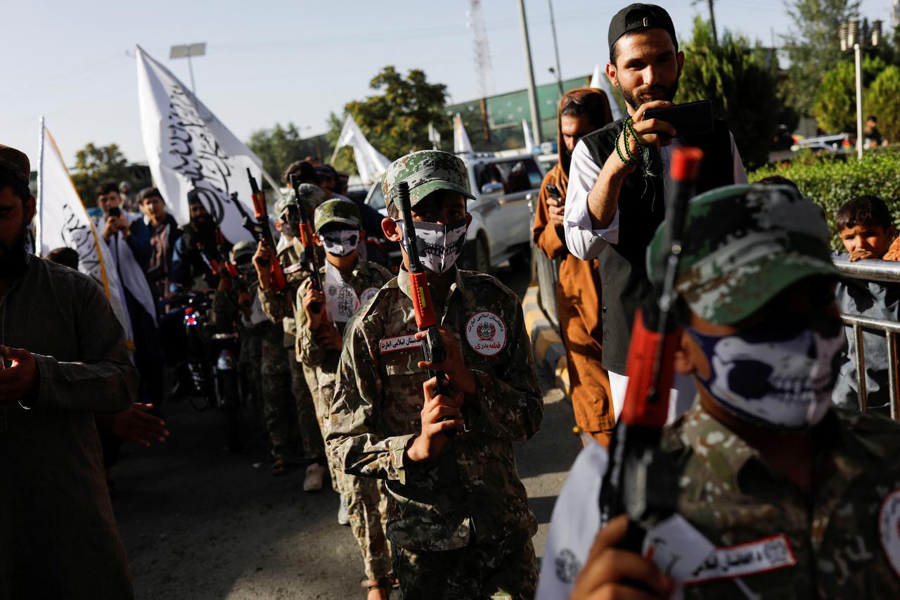 Afghan children, dressed in military uniforms, hold toy weapons on the second anniversary of the fall of Kabul at a street near the U.S. embassy in Kabul