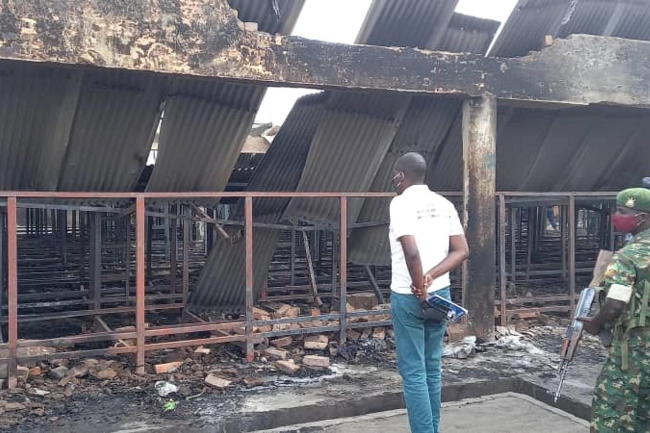 A journalist, policeman and a soldier observe the damage in front of the main prison after the fire, in Gitega