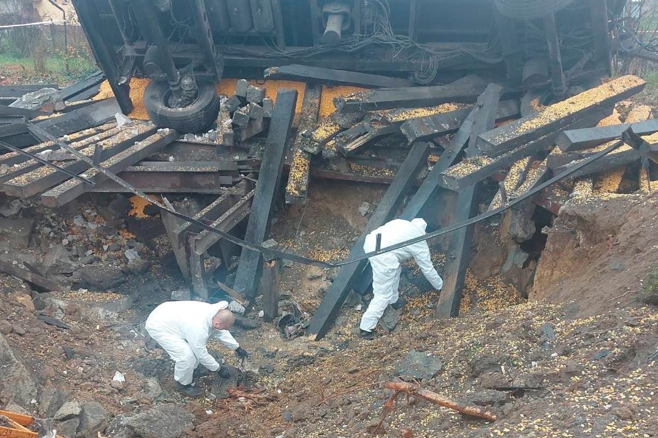 Crew members look through a crater next to an overturned vehicle at the site of an explosion in Przewodow