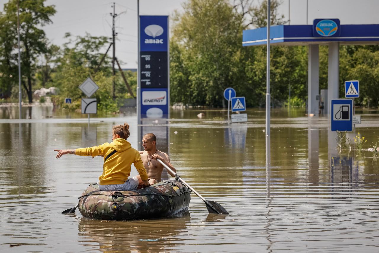 Local residents sail on a boat at a street during an evacuation from a flooded area after the Nova Kakhovka dam breached in Kherson
