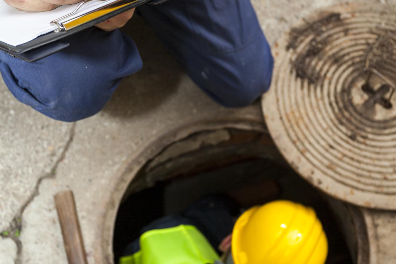 Two manual hard workers on field writing down the water inside of manhole at the road. Detail, view from above.Two manual hard workers on field writing down the water inside of manhole at the road. Detail, view from above.