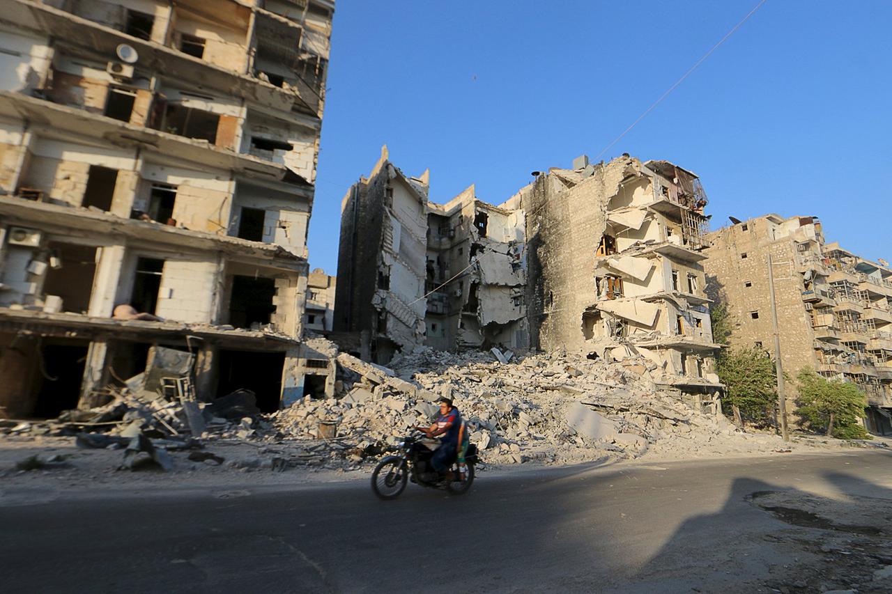Residents ride a motorcycle past damaged buildings in a rebel-controlled area of Aleppo, Syria July 24, 2015. Picture taken July 24, 2015. REUTERS/Abdalrhman Ismail