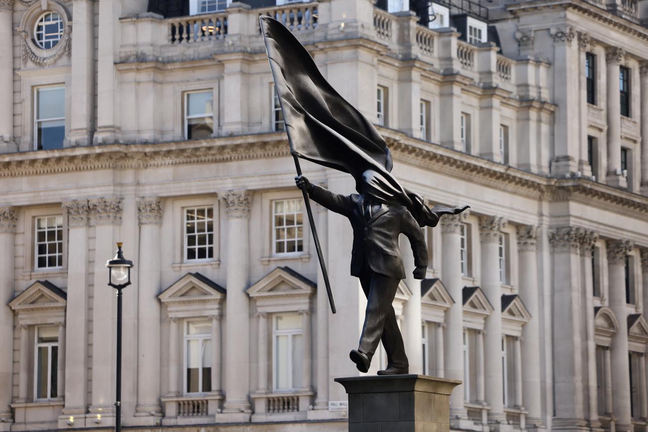 A statue depicting a person stepping off the plinth while carrying a flag covering their face, by British street artist Banksy, stands in London